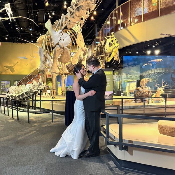Joyful bride and groom pose before dinosaur skeleton, highlighting unique wedding in Dallas, TX