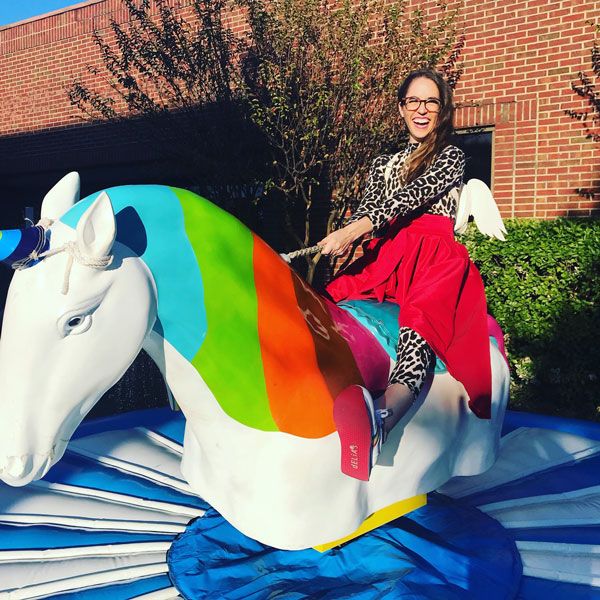 Woman rides colorful mechanical unicorn at carnival, with festive décor in Dallas, TX